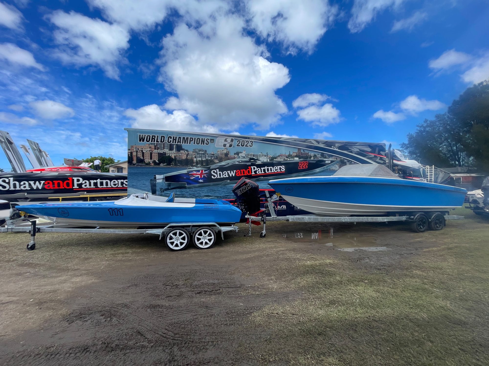 Two blue Jackson Craft boats on trailers in the pits, the Excite V-21 (race number 111) in front and the larger Apex V-28 behind